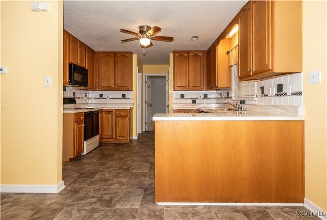 Kitchen featuring electric stove, black microwave, a peninsula, ceiling fan, and backsplash | Image 8