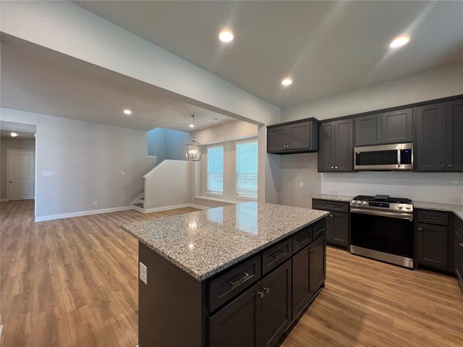 Kitchen with appliances with stainless steel finishes, light wood-style floors, light stone counters, a center island, and open floor plan | Image 8