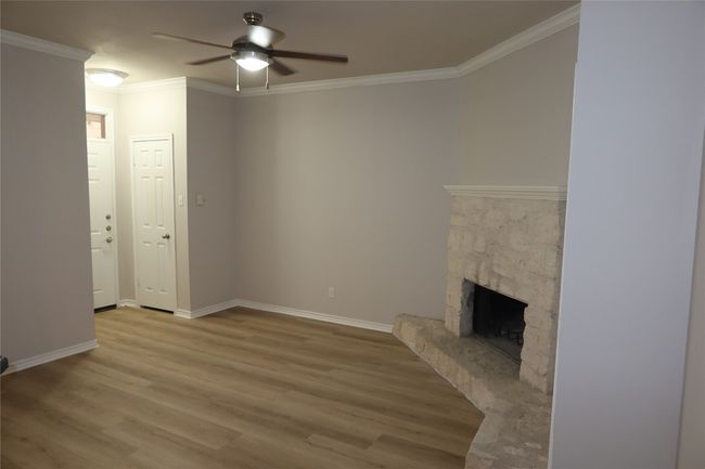 Unfurnished living room featuring ceiling fan, wood finished floors, crown molding, a fireplace, and baseboards | Image 5