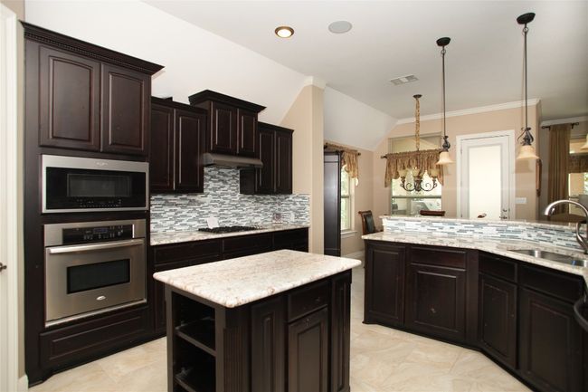 Kitchen featuring appliances with stainless steel finishes, a sink, backsplash, vaulted ceiling, and hanging light fixtures | Image 11