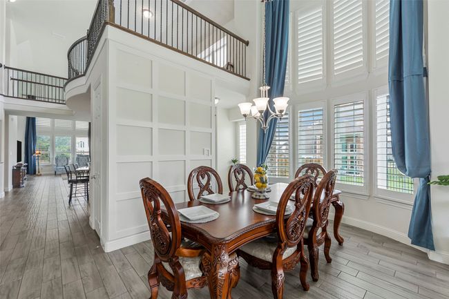 Dining space featuring a towering ceiling, wood finished floors, a chandelier, baseboards, and stairway | Image 9