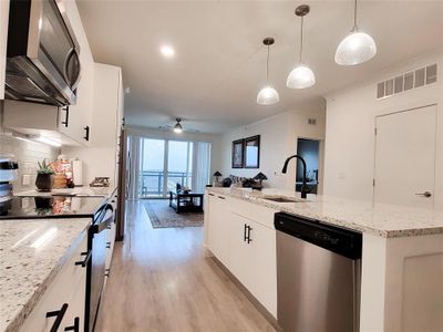 Kitchen with hanging light fixtures, a center island, light wood-type flooring, stainless steel appliances, and white cabinetry | Image 2