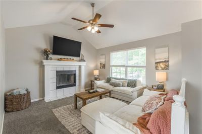 Living room with light colored carpet, ceiling fan, a tiled fireplace, and vaulted ceiling | Image 1