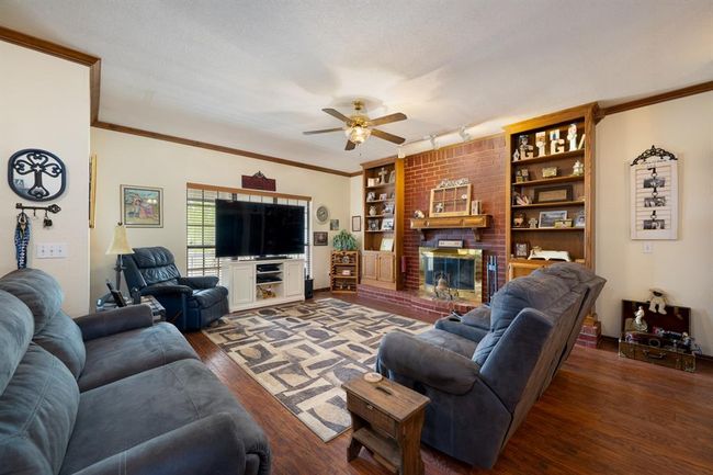 Living area with wood finished floors, crown molding, a fireplace, and ceiling fan | Image 9
