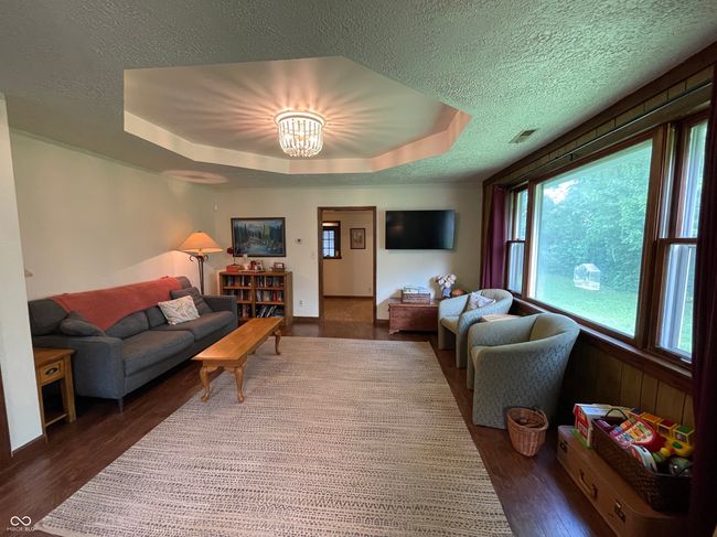 living area with a textured ceiling, a raised ceiling, wood finished floors, and a chandelier | Image 16