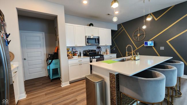 kitchen with appliances with stainless steel finishes, a kitchen bar, light wood-type flooring, and white cabinetry | Image 5