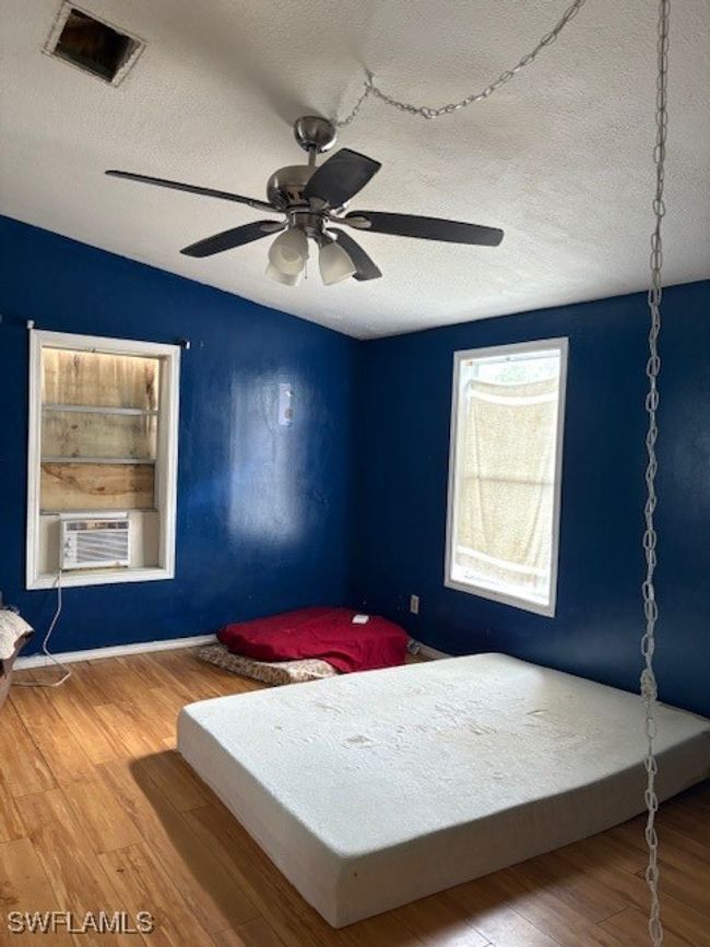 Bedroom featuring a textured ceiling, cooling unit, wood finished floors, a ceiling fan, and baseboards | Image 4