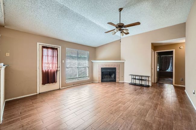 Unfurnished living room with a textured ceiling, wood finished floors, ceiling fan, and a fireplace | Image 4