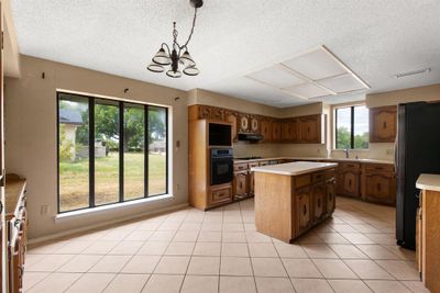 Kitchen featuring a kitchen island, an inviting chandelier, decorative light fixtures, stainless steel refrigerator, and black oven | Image 3