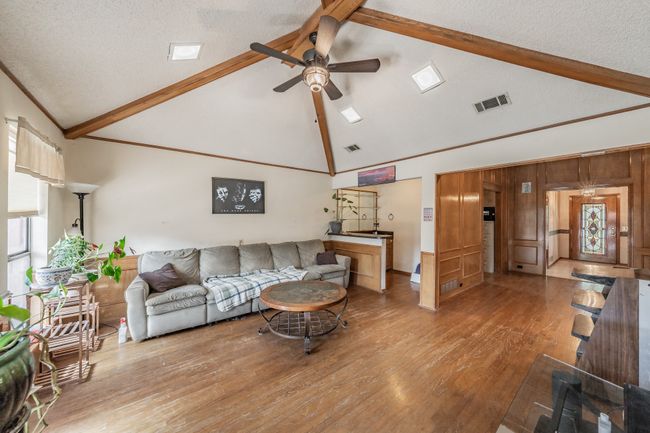 Living area featuring beamed ceiling, a ceiling fan, wood finished floors, high vaulted ceiling, and a textured ceiling | Image 6