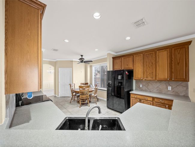 Kitchen with crown molding, visible vents, black refrigerator with ice dispenser, and a sink | Image 9