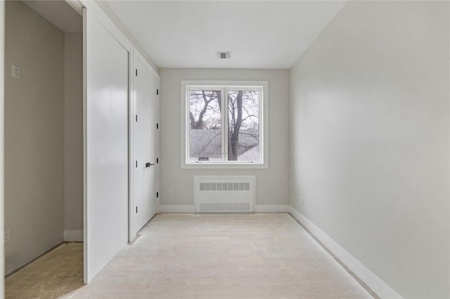 Empty room with radiator heating unit, baseboards, visible vents, and light wood-style floors | Image 23