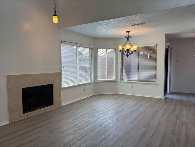 Unfurnished living room featuring wood finished floors, a textured ceiling, baseboards, a notable chandelier, and visible vents | Image 9
