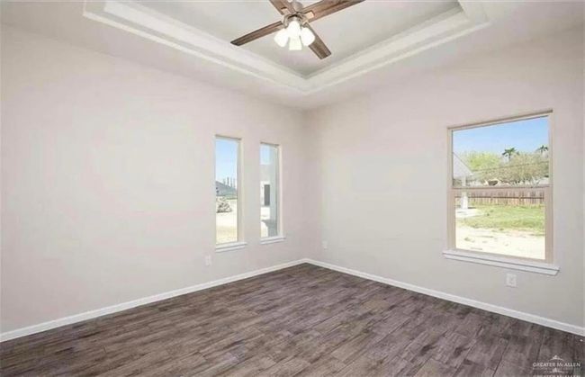 Unfurnished room featuring a tray ceiling, dark wood-style flooring, baseboards, ceiling fan, and crown molding | Image 5
