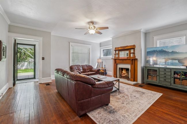 Living area featuring a ceiling fan, dark wood-type flooring, a large fireplace, and ornamental molding | Image 5