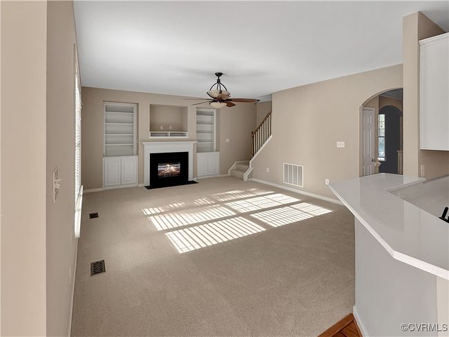 Unfurnished living room featuring a ceiling fan, arched walkways, built in features, a fireplace with flush hearth, and carpet flooring | Image 7