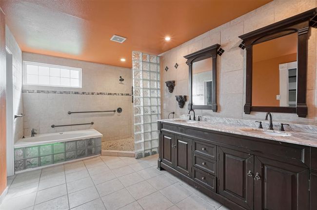 A show-stopping second bathroom featuring a deep soaking tub with glass block accents, a walk-in shower with pebble floor, and bold design choices including a vibrant ceiling and striking dark wood vanity. | Image 33