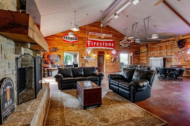 Living area featuring high vaulted ceiling, concrete floors, a fireplace, wood walls, and beam ceiling | Image 30