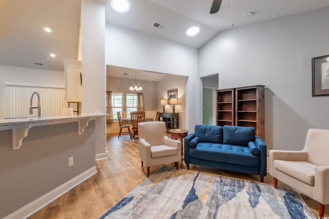 Living area with visible vents, baseboards, light wood finished floors, ceiling fan with notable chandelier, and high vaulted ceiling | Image 18