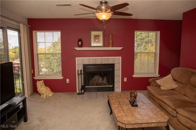 Carpeted living room with ceiling fan, a textured ceiling, and a tiled fireplace | Image 3