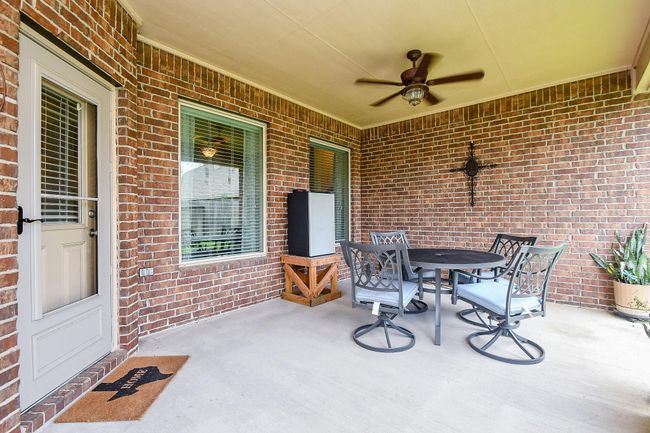 Outdoor patio with a brick wall, ceiling fan, and seating area. | Image 27
