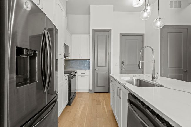 Kitchen with stainless steel appliances, a sink, light countertops, and white cabinets | Image 12