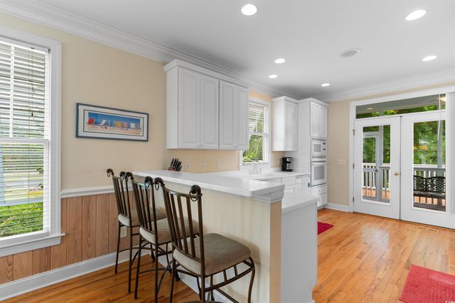 Kitchen with white appliances, ornamental molding, a kitchen bar, french doors, and white cabinets | Image 4