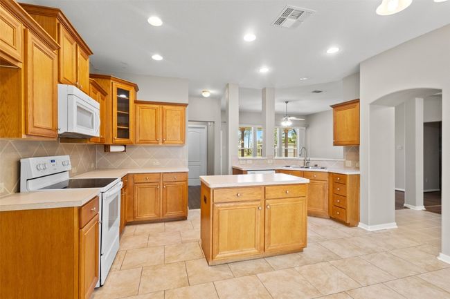Kitchen with white appliances, tasteful backsplash, recessed lighting, light countertops, and glass insert cabinets | Image 12