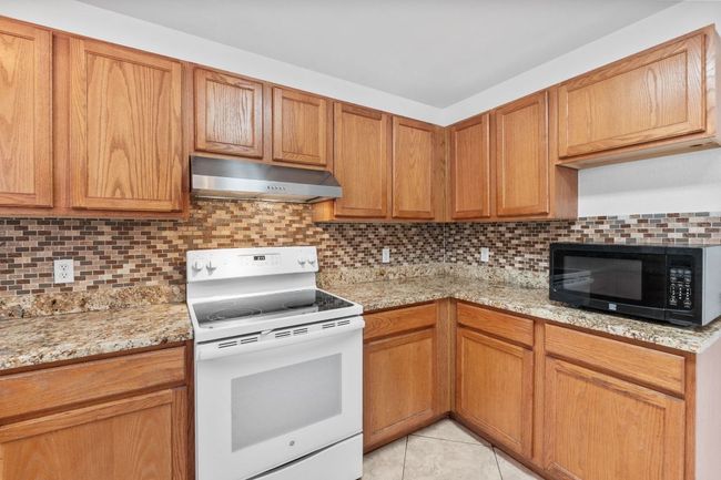 Kitchen featuring white electric range oven, black microwave, extractor fan, decorative backsplash, and light stone counters | Image 14