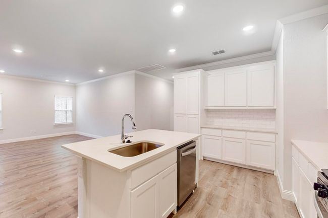 Kitchen with sink, dishwasher, a kitchen island with sink, backsplash, and white cabinets | Image 6