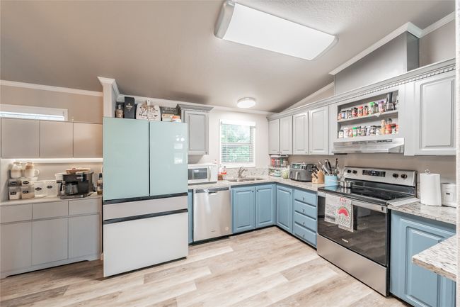 Kitchen featuring appliances with stainless steel finishes, crown molding, blue cabinets, lofted ceiling, and light wood-type flooring | Image 8