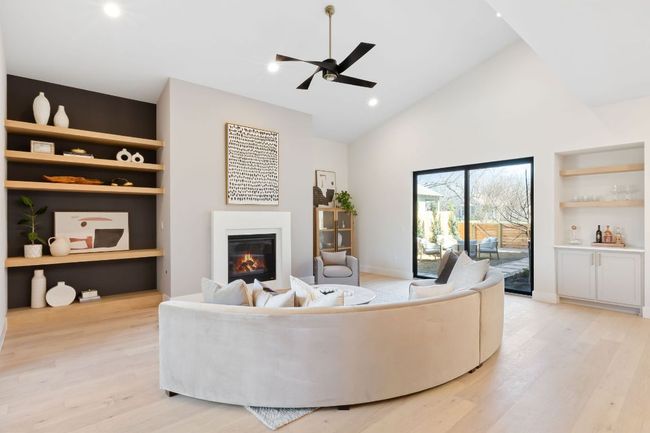 Living area featuring a glass covered fireplace, high vaulted ceiling, light wood-type flooring, and built in features | Image 20