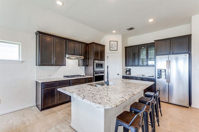 Kitchen with appliances with stainless steel finishes, dark brown cabinets, tasteful backsplash, light tile patterned flooring, and lofted ceiling | Image 7