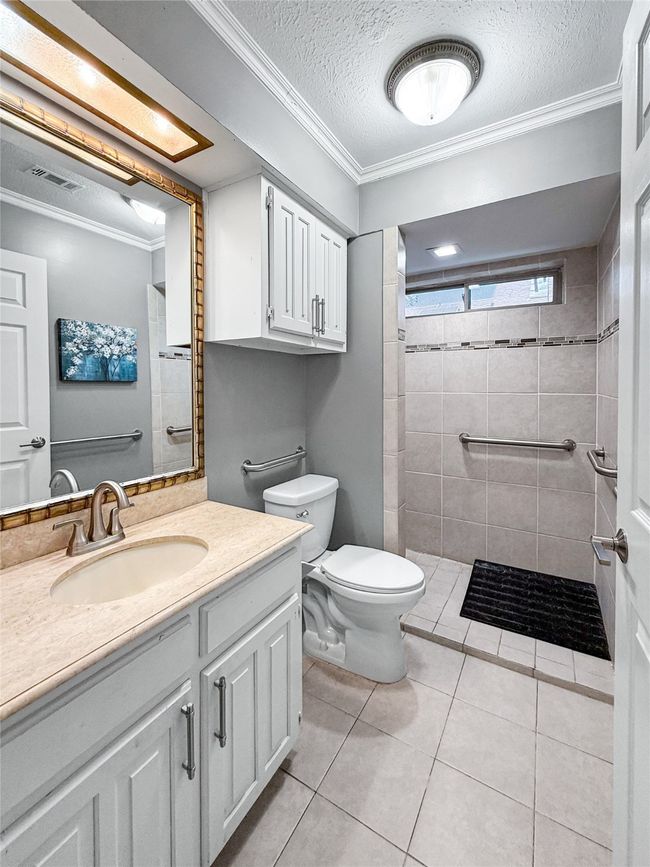Bathroom with ornamental molding, a textured ceiling, tile patterned floors, vanity, and a tile shower | Image 18