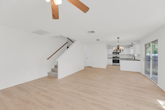 Unfurnished living room featuring light wood finished floors, a sink, stairway, and ceiling fan with notable chandelier | Image 6