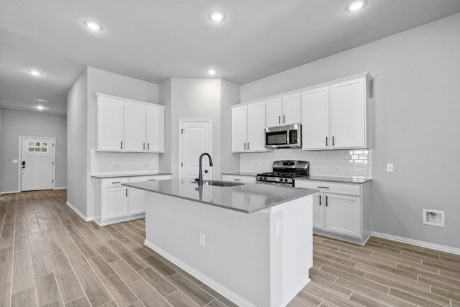 Kitchen featuring baseboards, a sink, appliances with stainless steel finishes, an island with sink, and light wood finished floors | Image 9