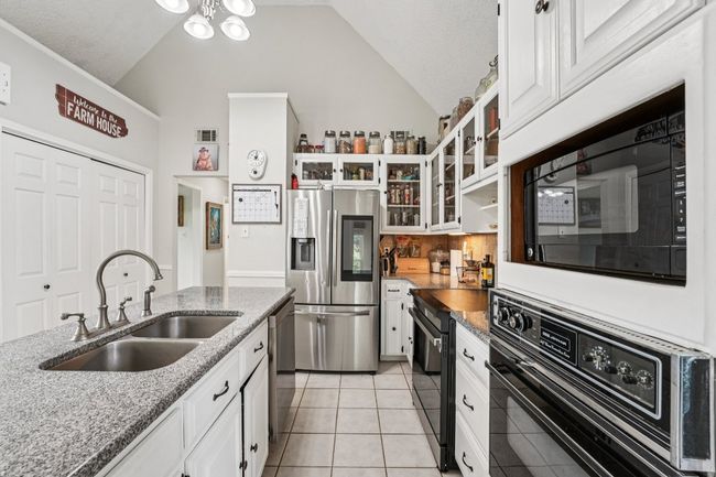 Kitchen featuring black appliances, high vaulted ceiling, white cabinets, light stone countertops, and light tile patterned flooring | Image 12