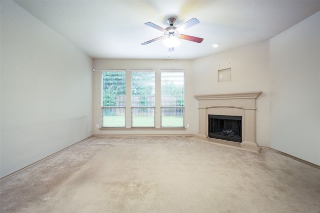 Unfurnished living room featuring a ceiling fan, carpet flooring, and a fireplace with raised hearth | Image 6