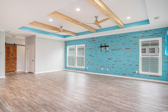 Spare room featuring ceiling fan, wallpapered walls, wood finished floors, a barn door, and beamed ceiling | Image 7