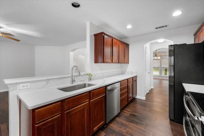 Kitchen with appliances with stainless steel finishes, arched walkways, a ceiling fan, light stone countertops, and dark wood finished Tile floors | Image 6
