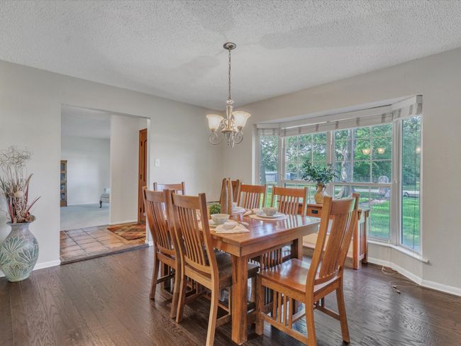 Dining room with healthy amount of natural light, wood finished floors, a chandelier, a textured ceiling, and baseboards | Image 6