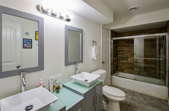 Full bathroom with a textured wall, bath / shower combo with glass door, vanity, and tile patterned floors | Image 24