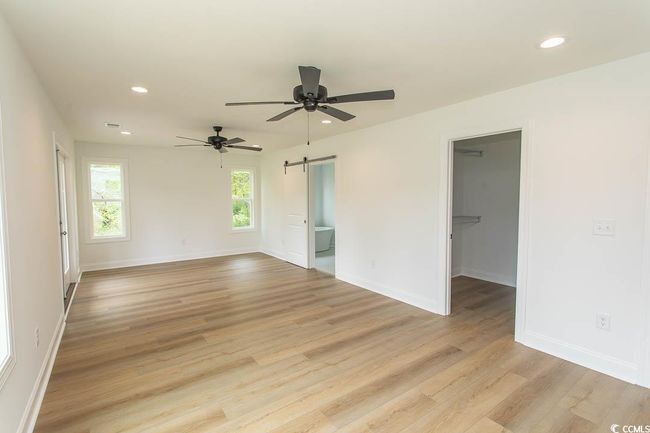 Master room featuring a barn door, recessed lighting, light wood-type flooring, ceiling fan, and baseboards | Image 22