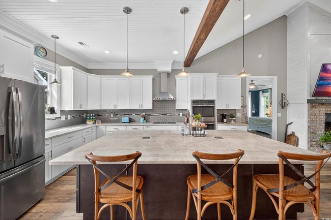 Kitchen with appliances with stainless steel finishes, wall chimney range hood, a center island, dark wood finished floors, and backsplash | Image 11