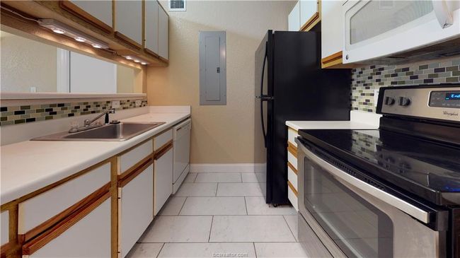 Kitchen featuring white appliances, a sink, light countertops, backsplash, and electric panel | Image 4