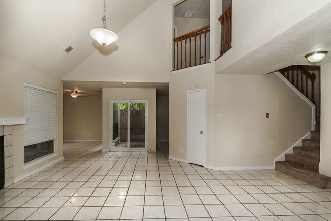 Unfurnished living room featuring high vaulted ceiling, stairs, ceiling fan, light tile patterned flooring, and a glass covered fireplace | Image 19