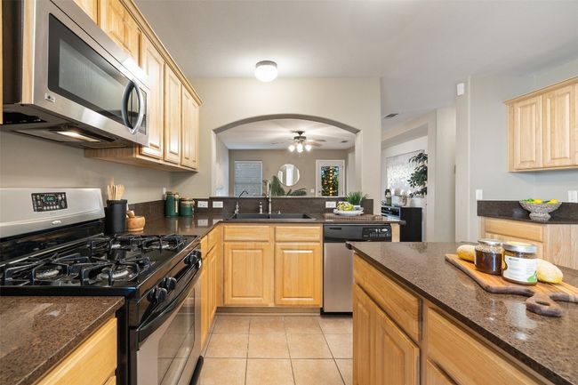 Kitchen featuring appliances with stainless steel finishes, arched walkways, light brown cabinetry, a sink, and light tile patterned floors | Image 12