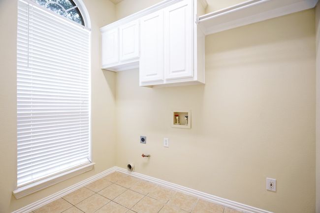 Laundry room, washer dryer hook up, baseboards, light tile patterned flooring, and cabinet space | Image 23