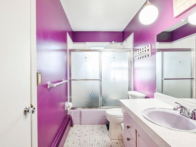 Full bathroom featuring a baseboard radiator, tile patterned flooring, enclosed tub / shower combo, toilet, and vanity | Image 10