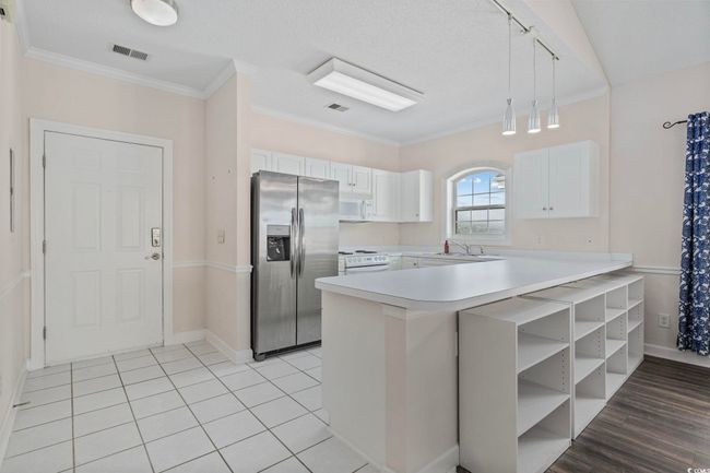 Kitchen featuring white appliances, a peninsula, light countertops, a sink, and white cabinetry | Image 4